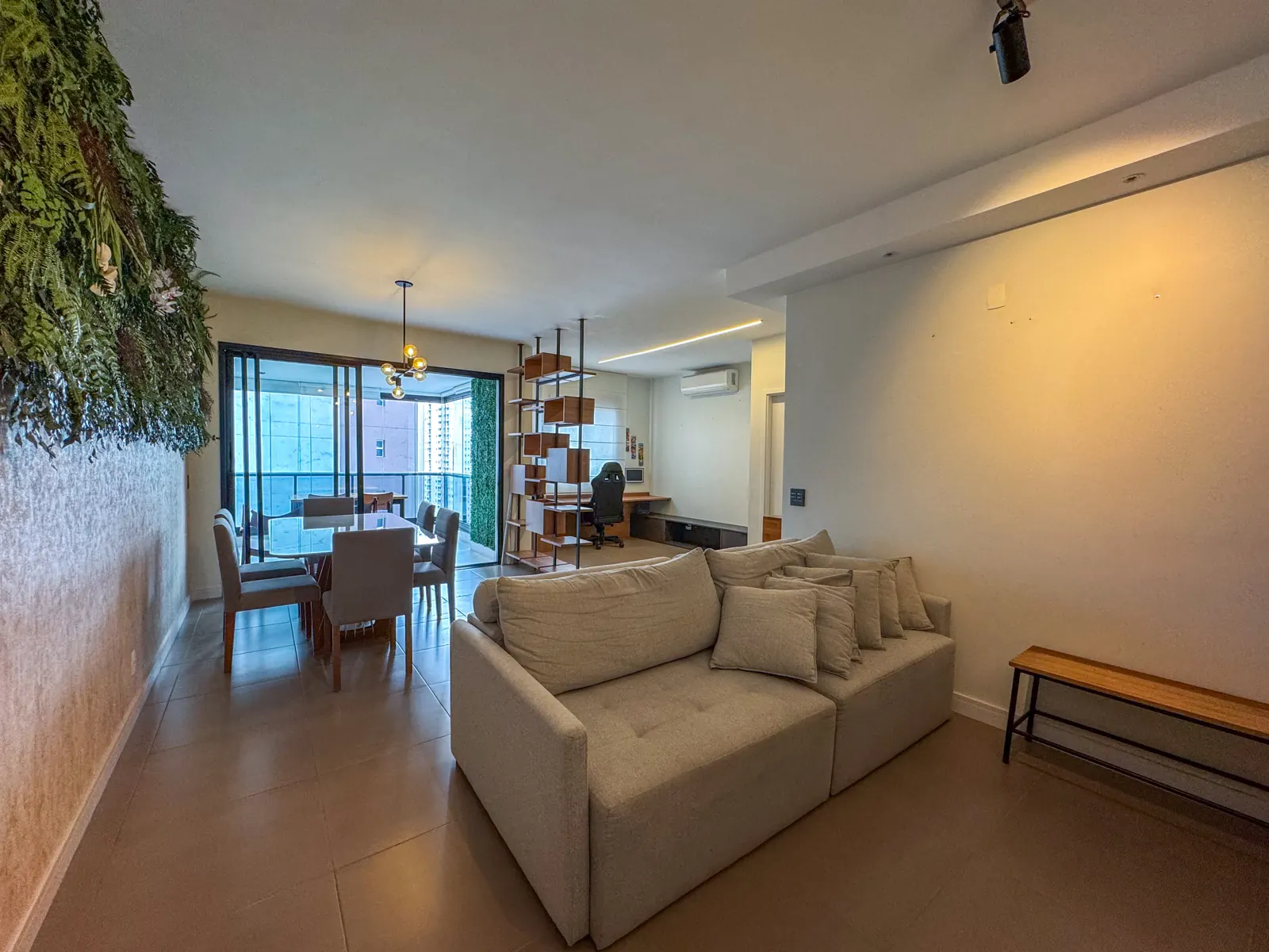 Sala de estar com sofá claro, jardim vertical e varanda ao fundo