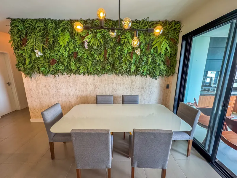 Mesa de jantar sob pendente dourado, com jardim vertical e porta para a varanda