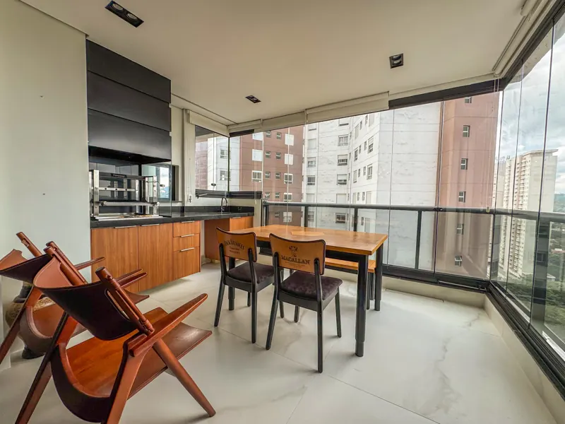 Varanda gourmet com churrasqueira, mesa de madeira e vista do andar alto