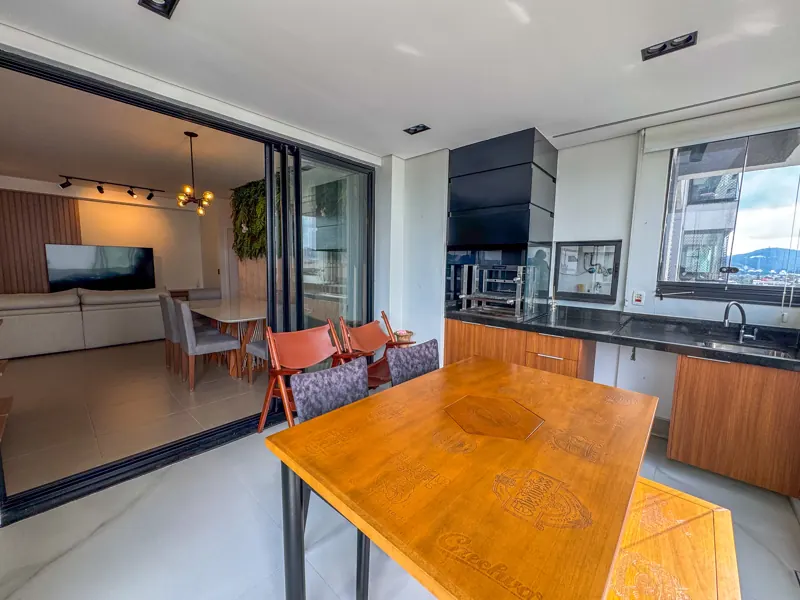 Varanda gourmet com mesa de madeira e a sala ao fundo